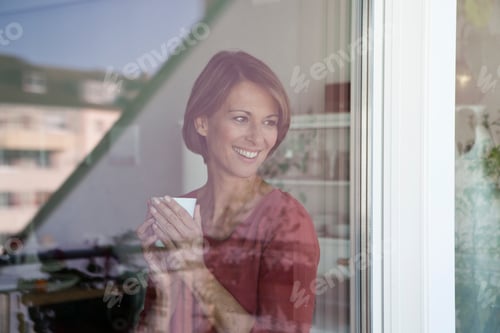 Preview: Smiling woman holding cup looking out of window