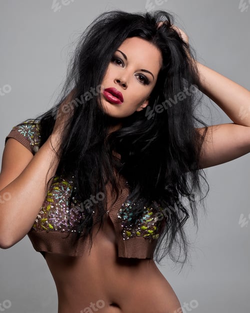 Preview: Glamorous woman with long black hair posing in a sequined brown top against a grey background.