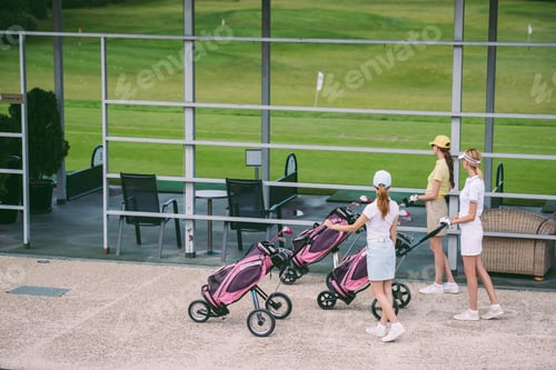 Preview: side view of female golfers with golf gear walking at golf course on summer day