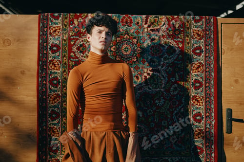 Preview: A stylish young man in a brown turtleneck top poses confidently against a rich patterned rug