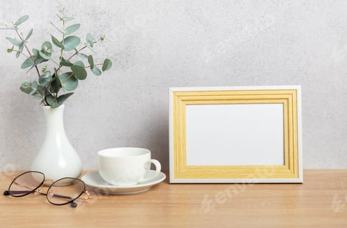 Preview: Eucalyptus branches, coffee cup, eyeglasses and empty photo frame creating cozy atmosphere on table