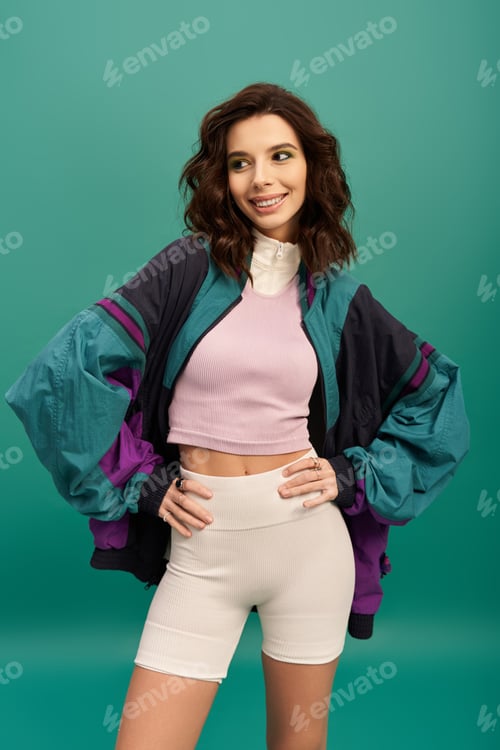 Preview: Stylish young woman showcases trendy sporty fashion against a vibrant turquoise backdrop