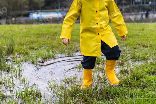 Preview: A child in a yellow raincoat is standing in a puddle of water
