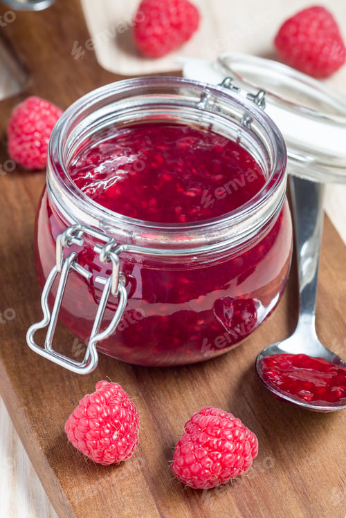 Preview: Raspberry jam in glass jar on a wooden board, vertical