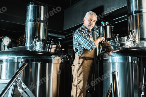 Preview: professional male brewer in overalls working in brewery