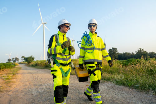 Preview: Two of wind turbine or windmill workers or technicians carry tools and walk along the road in field