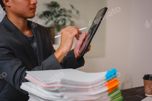 Preview: A businessman sits at his desk, working late into night on his laptop.reviews documents carefully