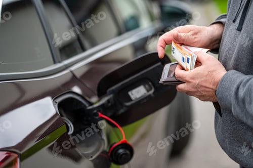 Preview: a man counts money standing at an open fuel tank, the concept of rising fuel prices, closeup