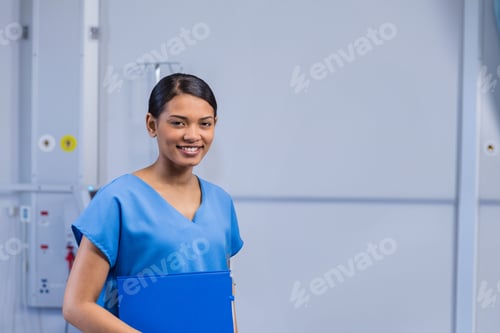 Preview: Young nurse smiling and holding blue folder in hospital corridor, next to medical panel, copy space