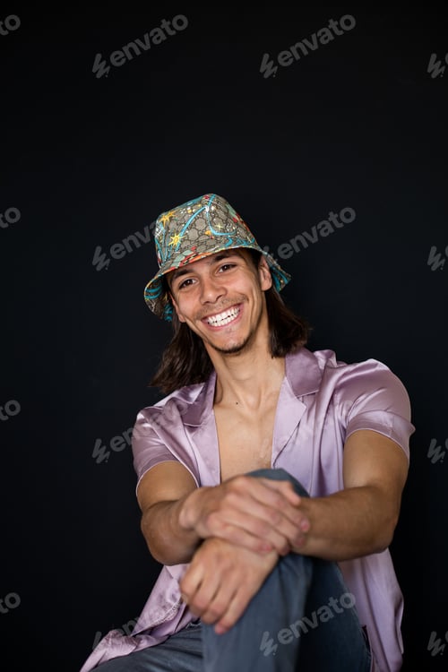 Preview: Gen z young man wearing a hat and smiling with his shirt open on a black background