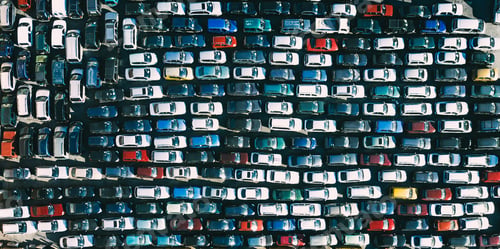 Preview: Aerial drone view of car lot full of cars, with various colors and models parked side by side