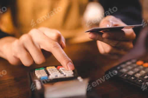 Preview: Closeup of young Asian barista wearing an orange apron uniform filling bank debit and credit card