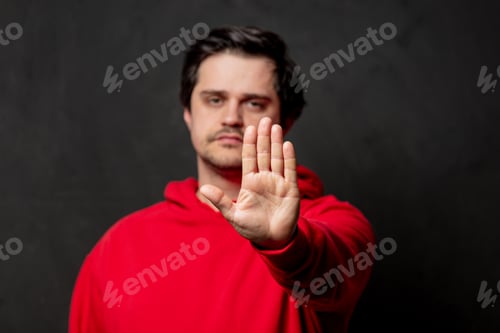 Preview: White guy in red sweatshirt show stop gesture on dark background