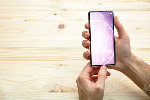 Preview: Man holding a smartphone, internet speed test on the screen, wooden background, copy space