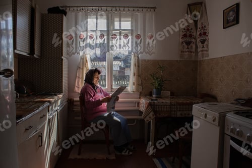 Senior Woman Relaxing in Kitchen Reading Newspaper
