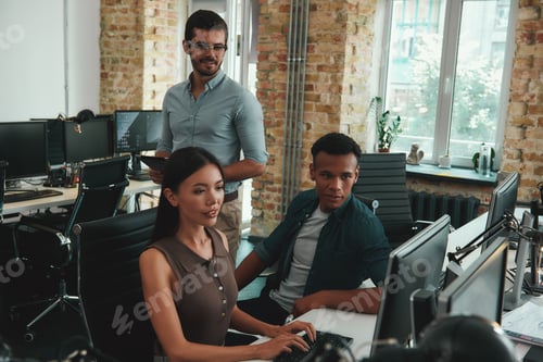 Preview: Focused on work. Group of young employees looking at computer monitor and discussing something while