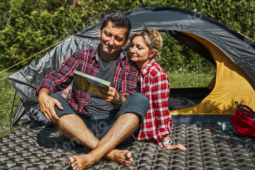 Preview: Couple planning next trip while sitting with map by tent. People relaxing at camping during summer