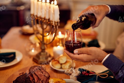 Preview: Close-up of Jewish man pouring wine while having meal at dining table on Hanukkah.