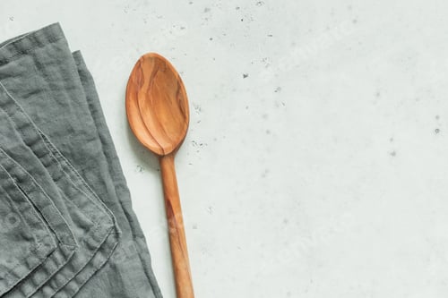 Preview: Wooden spoon and grey linen napkin on a white kitchen table. Top view, copy space.