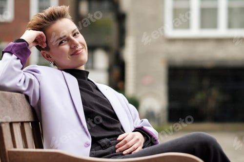 Preview: Friendly young woman sitting on a bench and looking at camera.