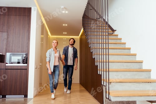 Vorschau: fröhliches Paar beim Händchenhalten in der Nähe der Treppe zu Hause