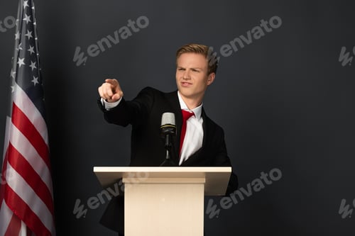 Preview: emotional man pointing with finger at camera on tribune with american flag on black background