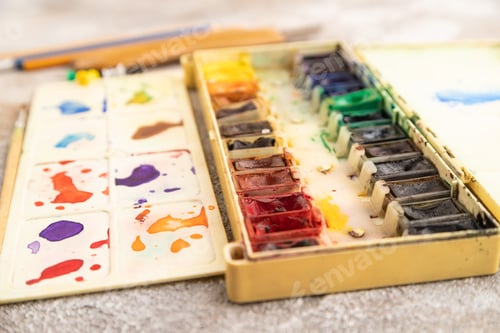 Preview: Drawing accessories set: brushes, pencils, watercolor on brown concrete. Side view, selective focus