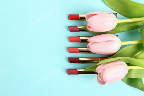 Preview: Bright lipsticks and spring flowers on light blue background, flat lay. Space for text