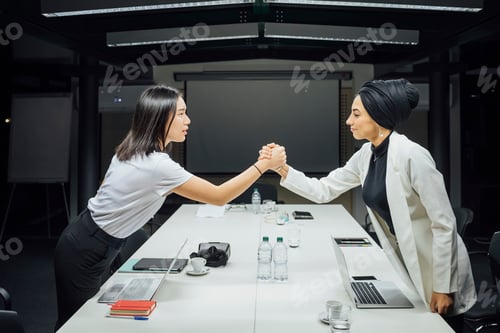 Preview: Businesswomen shaking hands over conference table