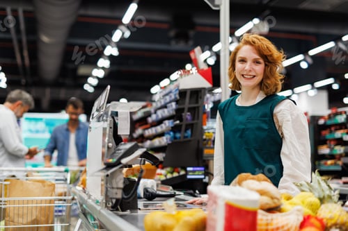Preview: Smiling cashier working at checkout counter in supermarket