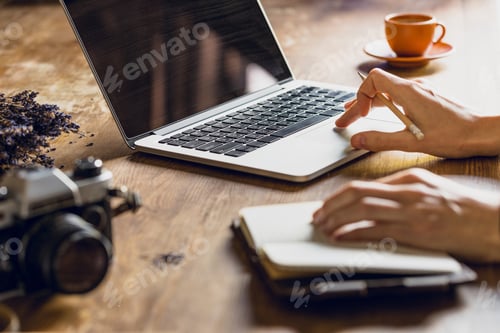 Preview: person using laptop and diary at workspace with vintage photo camera