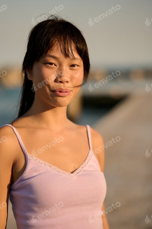 Preview: Young asian woman smiling at golden hour on pier