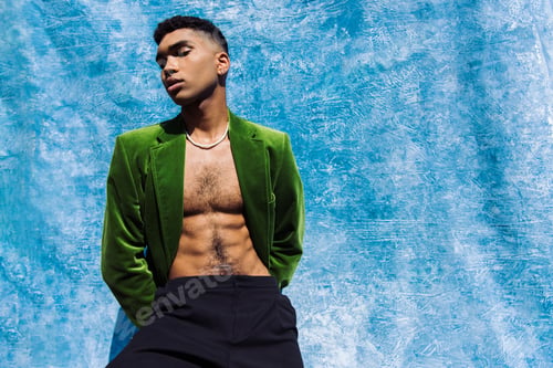Preview: young african american man in fashionable green blazer posing with hands behind back near blue drape
