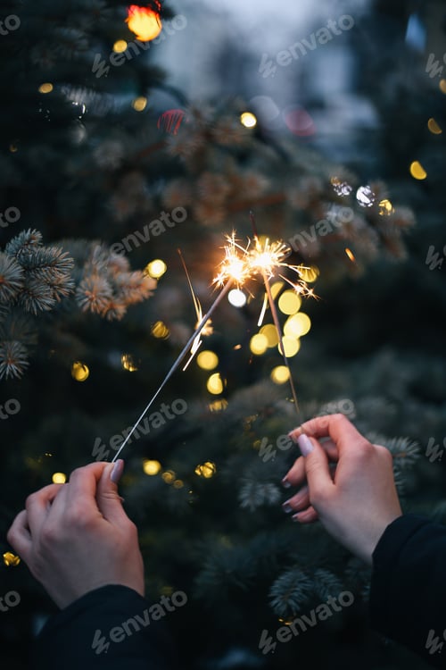 Preview: girl's hand holding sparklers on the background of a Christmas tree with lights