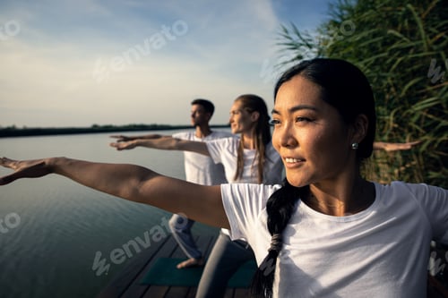 Preview: Group of people doing yoga exercises by the lake at sunset.