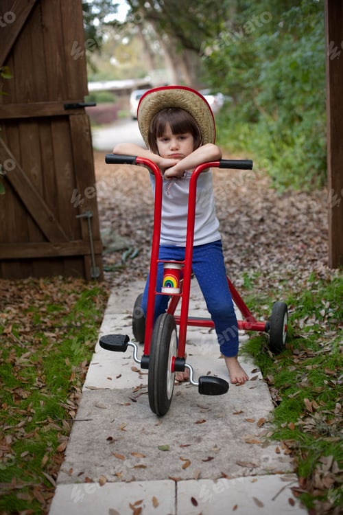 Preview: Portrait of four year old girl sitting on her tricycle in garden