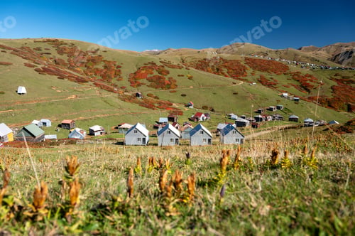Preview: Beautiful autumn mountain landscape with colorful trees, snow peaks and houses.