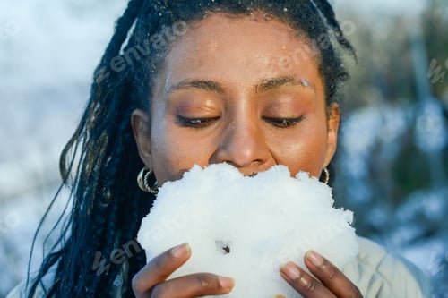 Preview: portrait stylish black young woman model play with snow in face confidently in snowy landscape