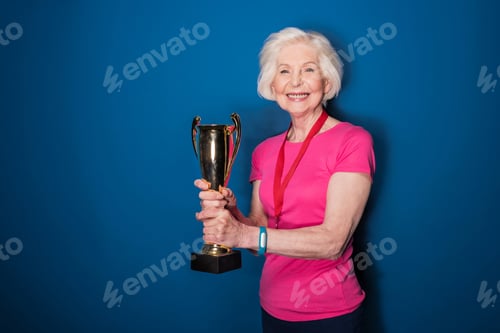 Preview: Happy senior sportswoman holding trophy isolated on blue