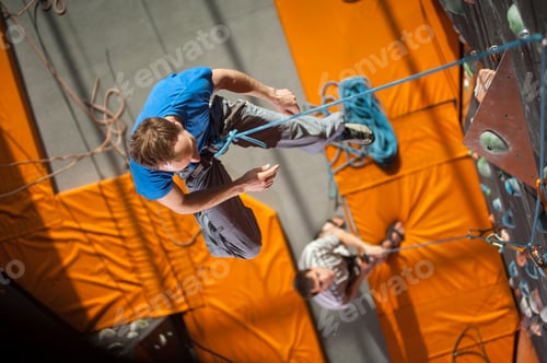 Preview: Male rock-climber practicing climbing on rock wall indoors