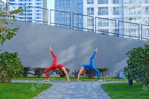 Preview: Young Attractive Woman In Red And Blue Sportswear Practices Yoga Exercises Outdoors.