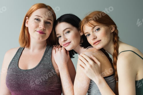 Preview: Body positive women in sportswear hugging plus size friend isolated on grey