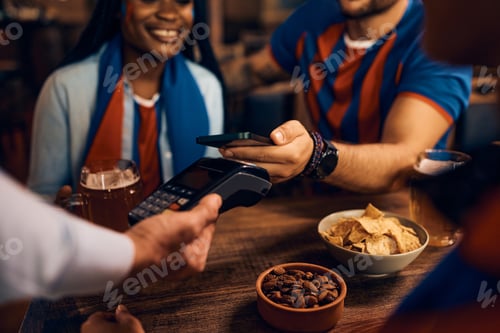 Preview: Close up of sports fan making contactless payment in a pub.