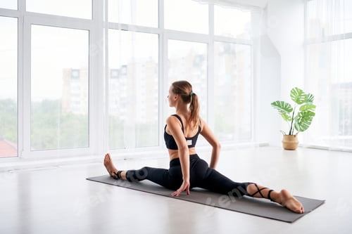 Preview: young beautiful woman doing yoga in a modern bright room with large windows. Yoga at home concept.