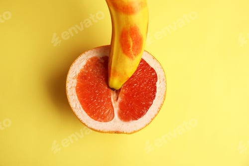 Preview: Fresh grapefruit and banana with red lipstick marks on yellow background, flat lay. Sex concept