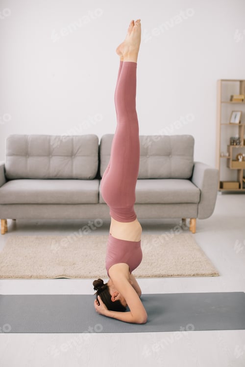 Preview: Attractive young woman stands on her head and upside down and doing fitness exercises at home.