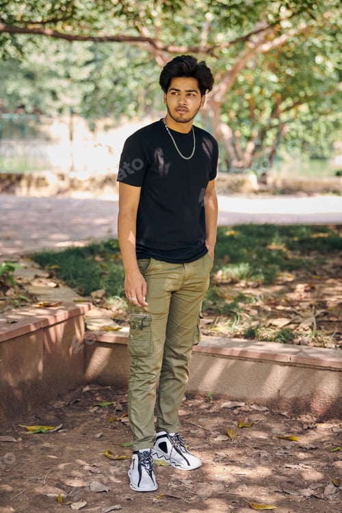 Preview: Attractive young indian man full height portrait in black t shirt, silver neck chain in green park