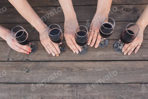 Preview: female hands hold glasses with red wine on a background of gray wooden boards.