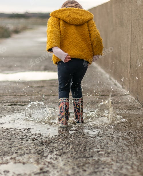 Preview: A little girl with rubber boots jumps into a puddle on a rainy day