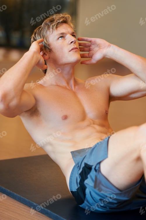 Preview: Working towards perfect abs. Fit young guy doing sit ups on a mat at the gym.
